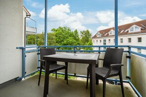 Un balcón con una mesa y dos sillas, con vistas a un conjunto de casas y árboles.