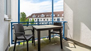 Ein Balkon mit Korbstühlen und einem Tisch, einem blauen Geländer und Blick auf eine Häuserreihe.