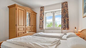 Ein Schlafzimmer mit zwei Betten, einem Kleiderschrank, einem Fenster mit Vorhängen und einem Nachttisch mit Lampe.