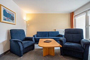 Ein Hotelzimmer mit zwei blauen Sesseln, einem Holztischchen, einem blauen Sofa, einem gerahmten Bild an der Wand und einer Stehlampe.