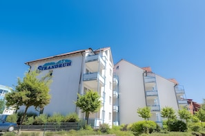 Un edificio de varios pisos con balcones, un letrero que dice 'Grandruth' y un cielo azul despejado.