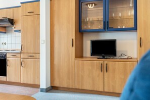 Una cocina con armarios de madera, estufa empotrada y un televisor sobre la encimera.
