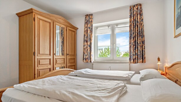A bedroom with two beds, a wardrobe, a window with curtains, and a nightstand with a lamp. - Apartment 'Ringstr. 21, 2. OG Links WE55' with Balcony and Wi-Fi (Binz)
