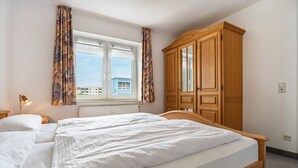 Ein Schlafzimmer mit einem Bett, einem Kleiderschrank, einem Fenster mit Vorhängen und einer Heizung.