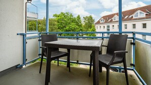 Ein Balkon mit Tisch und zwei Stühlen, der auf eine Häuserreihe und Bäume blickt.