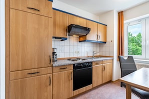 Cuina amb armaris de fusta, un rentaplats negre, una cuina i una finestra amb cortines.