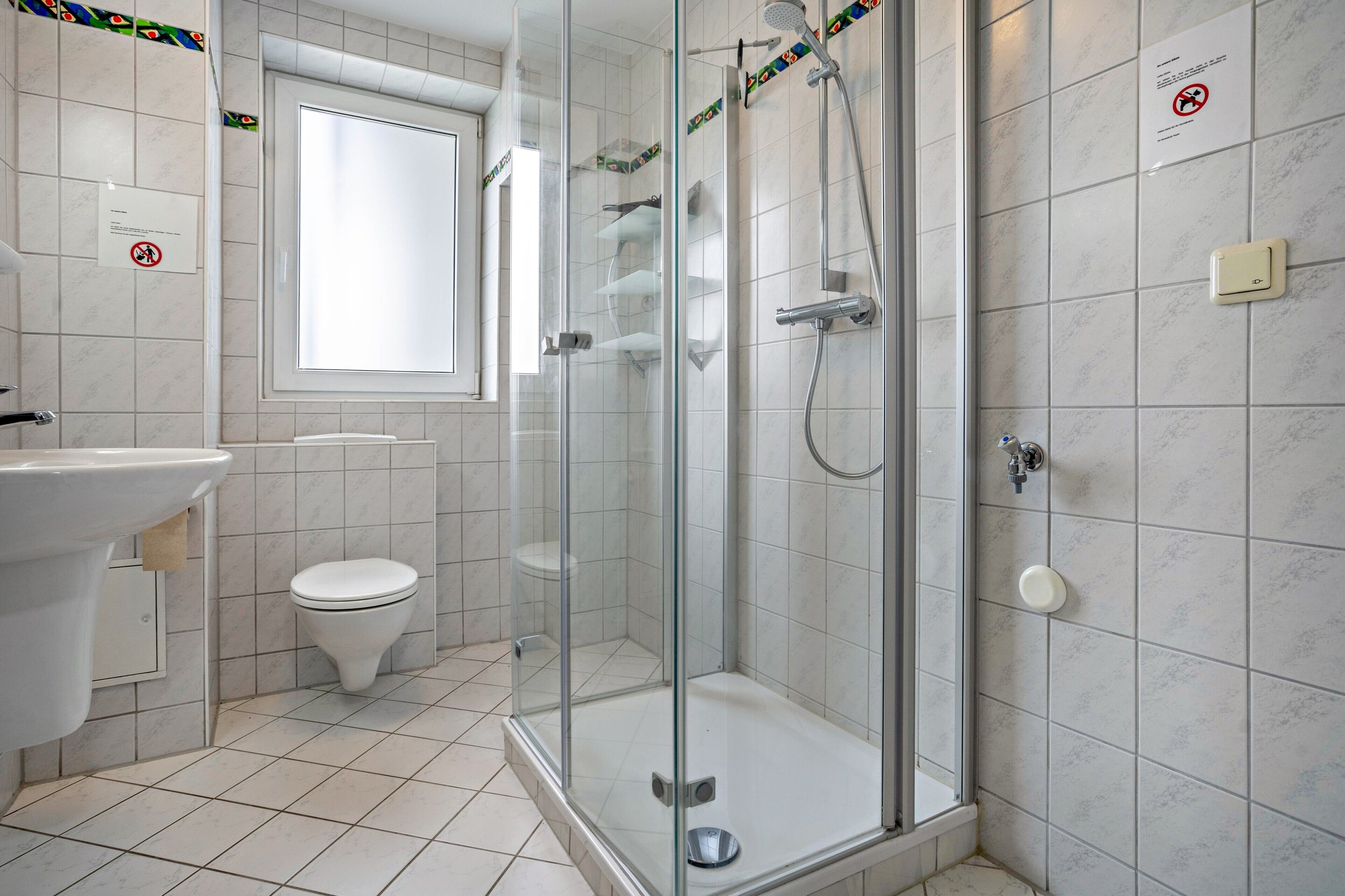 A bathroom with a glass-enclosed shower, a toilet, a sink, and a window.