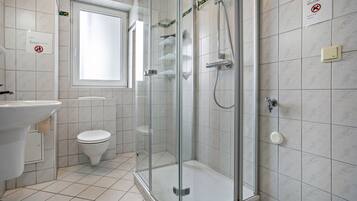 A bathroom with a glass-enclosed shower, a toilet, a sink, and a window.
