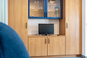 A wooden cabinet with a television on top, a glass-fronted upper section with items inside, and a blue object partially visible in the foreground. - Apartment 'Ringstr. 21, 1. OG Rechts WE54' with Balcony and Wi-Fi (Binz)
