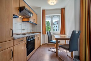 A compact kitchen with wooden cabinets, a stove, and a window with curtains. - Apartment 'Ringstr. 21, 1. OG Rechts WE54' with Balcony and Wi-Fi (Binz)
