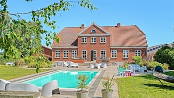 Uma grande casa de tijolos com piscina, área de estar externa e gramado bem cuidado.