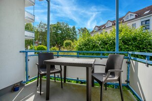 Ein Balkon mit Korbmöbeln, einem blauen Geländer und Blick auf Wohnhäuser und Grünflächen.