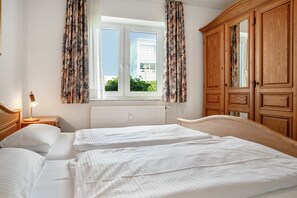 Ein Schlafzimmer mit zwei Betten, einem Fenster mit Vorhängen, einem Heizkörper und Holzmöbeln.