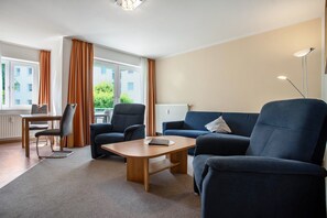 Ein modernes Hotelzimmer mit einer Sitzecke, Sesseln, einem kleinen Tisch, einem Schreibtisch und einem Fenster mit Vorhängen.