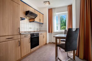 Une cuisine avec des meubles de rangement en bois, une cuisinière et une table à manger avec une chaise.
