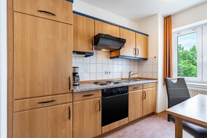 Eine Küche mit Holzausstattung, einem schwarzen Geschirrspüler, einem Herd und einem Fenster mit Vorhängen.