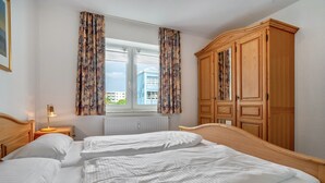 A bedroom with a large bed, wooden wardrobe, and a window with curtains. - Apartment 'Ringstr. 22, 1. OG Rechts WE44' with Balcony and Wi-Fi (Binz)