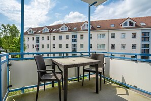 Een balkon met een tafel en stoelen, met uitzicht op een rij witte gebouwen met rode daken.