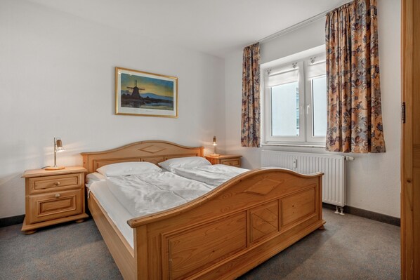 Een slaapkamer met een houten bed, nachtkastjes, een wandlamp en een aan de muur hangend schilderij.