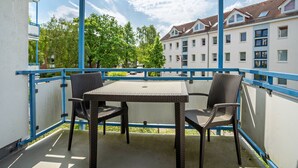 A balcony with a table and chairs, a blue railing, and a view of residential buildings. - Apartment 'Ringstr. 22, 1. OG Rechts WE44' with Balcony and Wi-Fi (Binz)