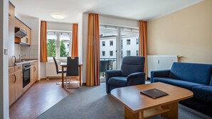 A hotel room with a kitchenette, a dining area, a sofa, and a view of buildings. - Apartment 'Ringstr. 22, 1. OG Rechts WE44' with Balcony and Wi-Fi (Binz)