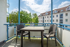 Ein Balkon mit Tisch und Stühlen, einem blauen Geländer und Blick auf Wohnhäuser.