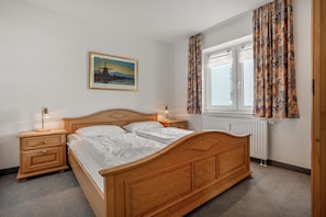 Ein Schlafzimmer mit einem hölzernen Bett, Nachttischen, einem Fensterschrank und einem an der Wand hängenden Bild.