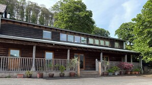 A wooden building with a porch, multiple windows, and potted plants. - Willow Cottage (Presteigne)