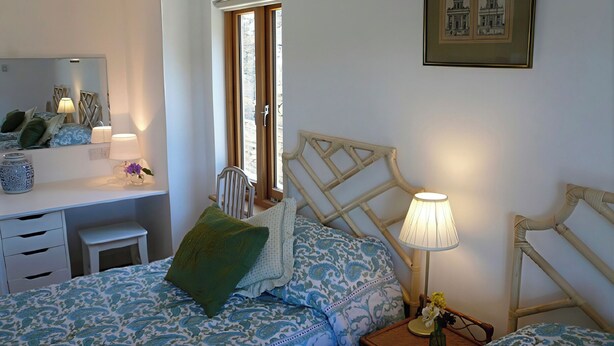 A bedroom with a bed, bedside table, lamp, chair, and a window with a view. - Willow Cottage (Presteigne)