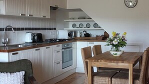 Cocina moderna con armarios blancos, encimera de madera y comedor con sillas de mimbre y una mesa de madera.