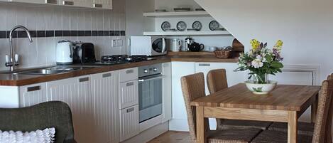 A modern kitchen with white cabinets, a wooden countertop, and a dining area with wicker chairs and a wooden table.