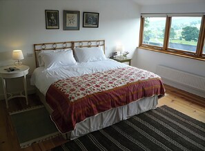 Ein Schlafzimmer mit einem Bett, zwei Nachttischen, einem Fenster mit Blick und drei gerahmten Bildern an der Wand.