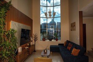 A living room with a large TV, a sofa, a coffee table, and a large window with a view of buildings. - Casa Mía : Private pool : 3 Bedrooms (cancun)