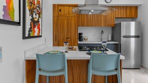 A modern kitchen with wooden cabinets, a stainless steel refrigerator, and a central island with two chairs. - Rooftop Pool & Ocean Views in Zona Romántica (Puerto Vallarta)