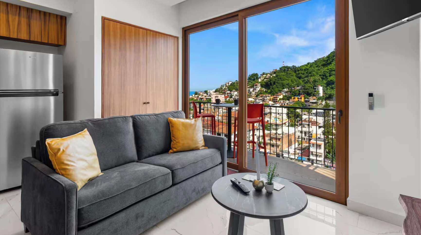 A modern living room with a grey sofa, a small round table, and a large sliding glass door to a balcony.