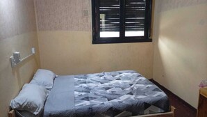 A single bed with a patterned bedspread, a window with horizontal blinds, and a wall-mounted air conditioning unit. - Punto 11 (Buenos Aires)