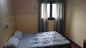 A small, single-bed room with a patterned bedspread, a window with curtains, and a wall-mounted light switch. - Punto 11 (Buenos Aires)