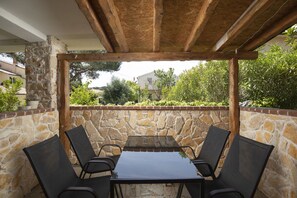 Een terras buiten, met een stenen muur, een houten pergola en een tafel met stoelen.
