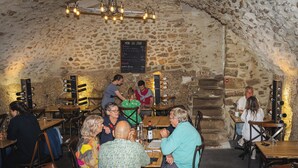 Un restaurant aux murs de pierre, avec des tables et des chaises, un tableau affichant le menu et un présentoir à bouteilles de vin.