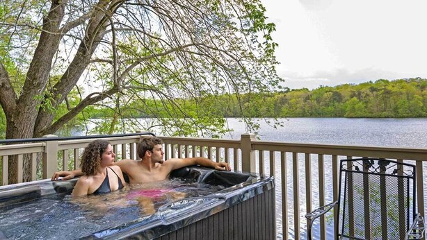 Een hottub op een terras met uitzicht op een meer en bomen.
