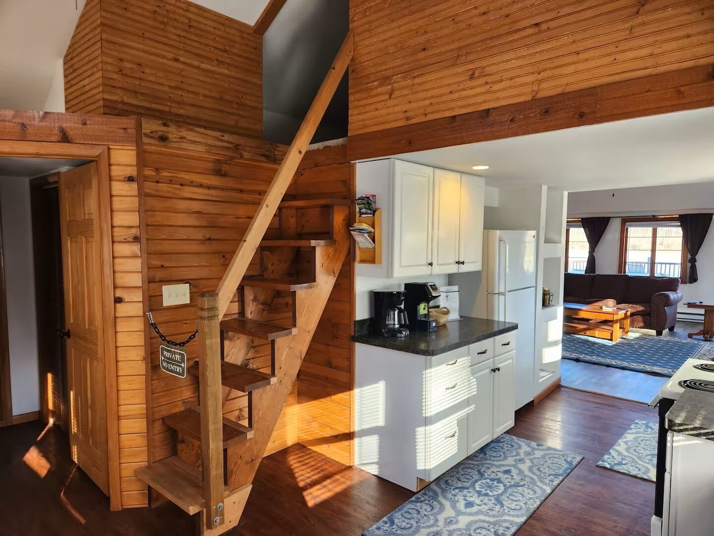 Un escalier en bois mène à une cuisine dotée de meubles blancs et à un coin repas comprenant un canapé et une table.
