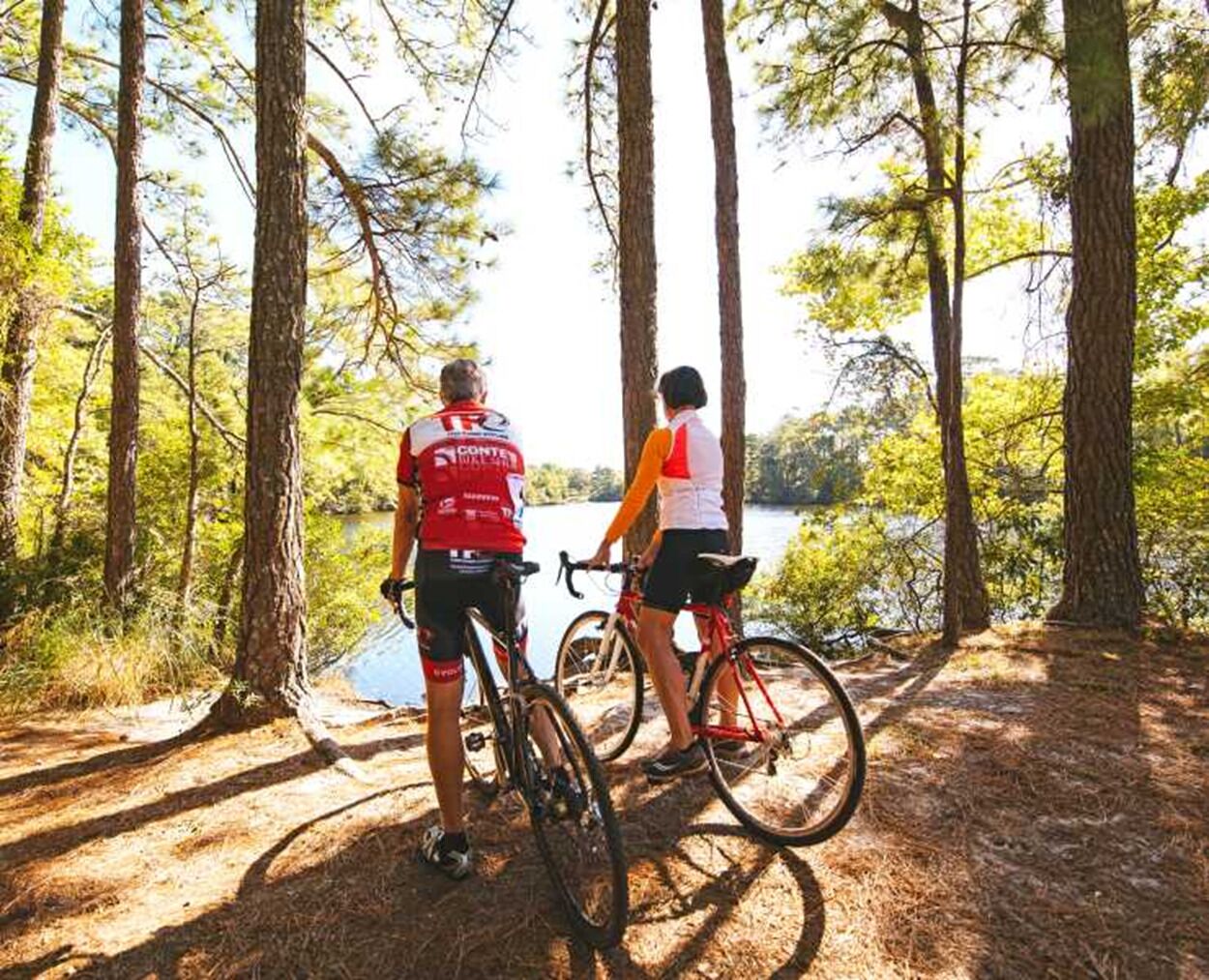 Deux personnes à vélo dans une zone boisée, avec un lac en arrière-plan.