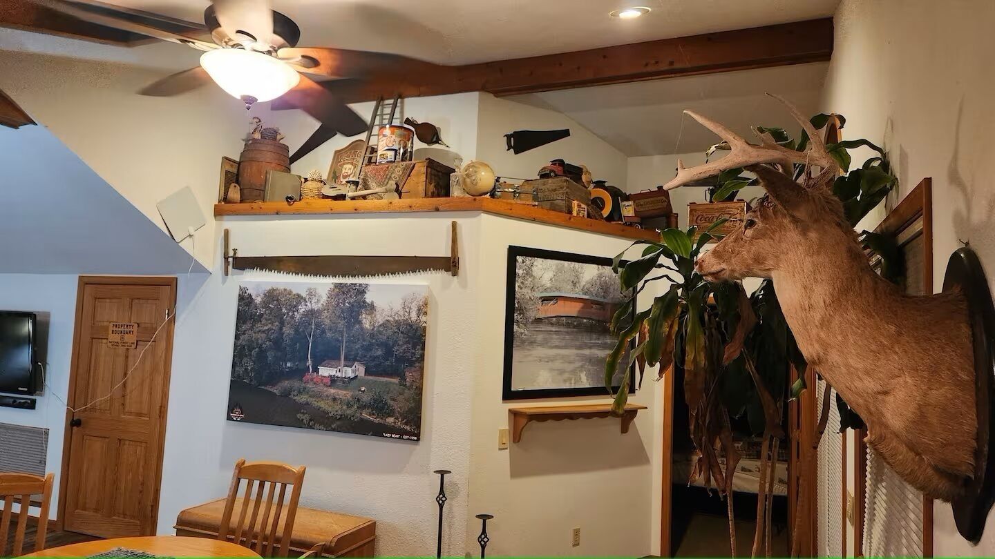 Ein Zimmer mit Deckenventilator, Holzregalen mit verschiedenen Gegenständen, einem aufgehängten Hirschkopf und gerahmten Bildern an den Wänden.