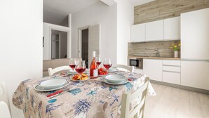 Ein Essbereich mit Tisch für vier Personen, eine Küche mit weißen Schränken und einer Wand mit Holzverkleidung.