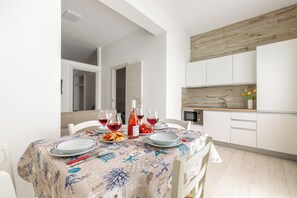 A dining area with a table set for four, a kitchen with white cabinets, and a wooden accent wall. - Borgo Climmena - Bilo con veranda (Manduria)