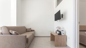 Ein modernes Wohnzimmer mit einer Couch, einem Couchtisch, einem flachbildfernseher an der Wand und einem Bett im Hintergrund.