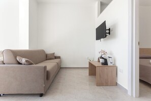 A modern living room with a sofa, a coffee table, a flat-screen TV mounted on the wall, and a bed in the background. - Borgo Climmena - Bilo con veranda (Manduria)