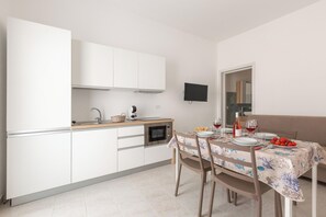 A modern kitchen with white cabinets, a microwave, and a dining table set for two with a tablecloth. - Borgo Climmena - Bilo con Patio (Manduria)