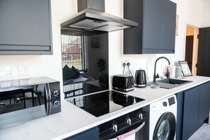 A compact kitchen with a built-in stove, a microwave, a toaster, a sink, and a washing machine. - Modern 1 Bedroom Apartment in Derby with Parking (Derby)