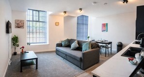 A modern living room with a sofa, a dining table, and a kitchen area. - Modern 1 Bedroom Apartment in Derby with Parking (Derby)